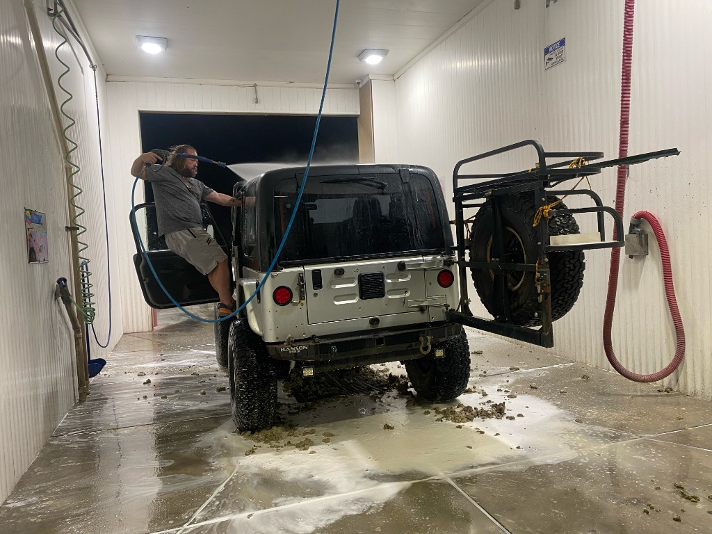 Rear view of the muddy Jeep in a car wash bay, clumps of playa mud on the floor