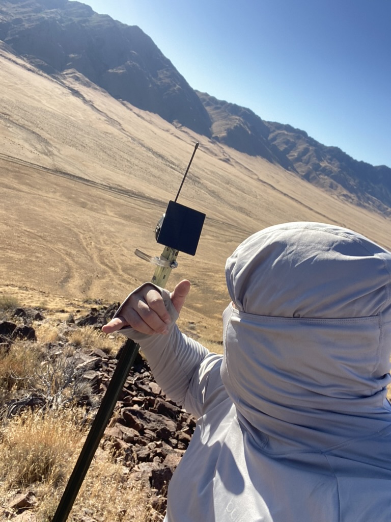 Ben holding a mesh repeater on the Poito mountainside, desert valley below